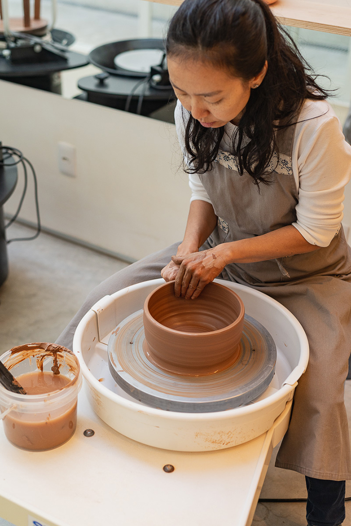 Cris Kim no ateliê, moldando peça no torno de cerâmica