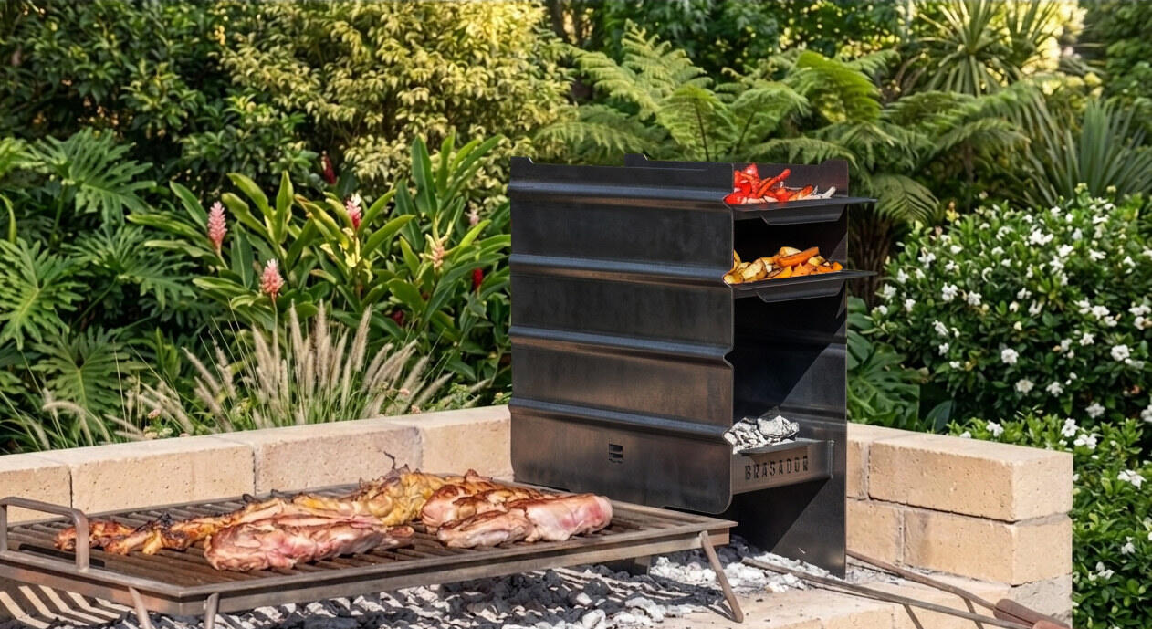 Brasador Esencial en un patio, con las bandejas cocinando morrones y verduras sobre el fuego y carne en la parrilla de al lado