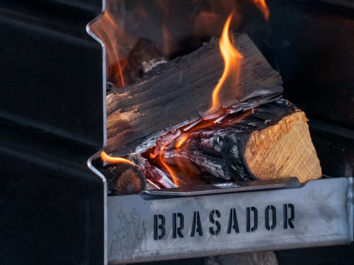 Leña ardiendo dentro del Brasador Esencial, con el logo grabado en la chapa del brasero