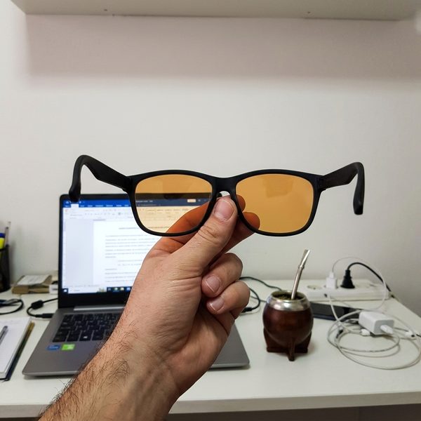 Blue blocker naranjas en la mano frente a la notebook