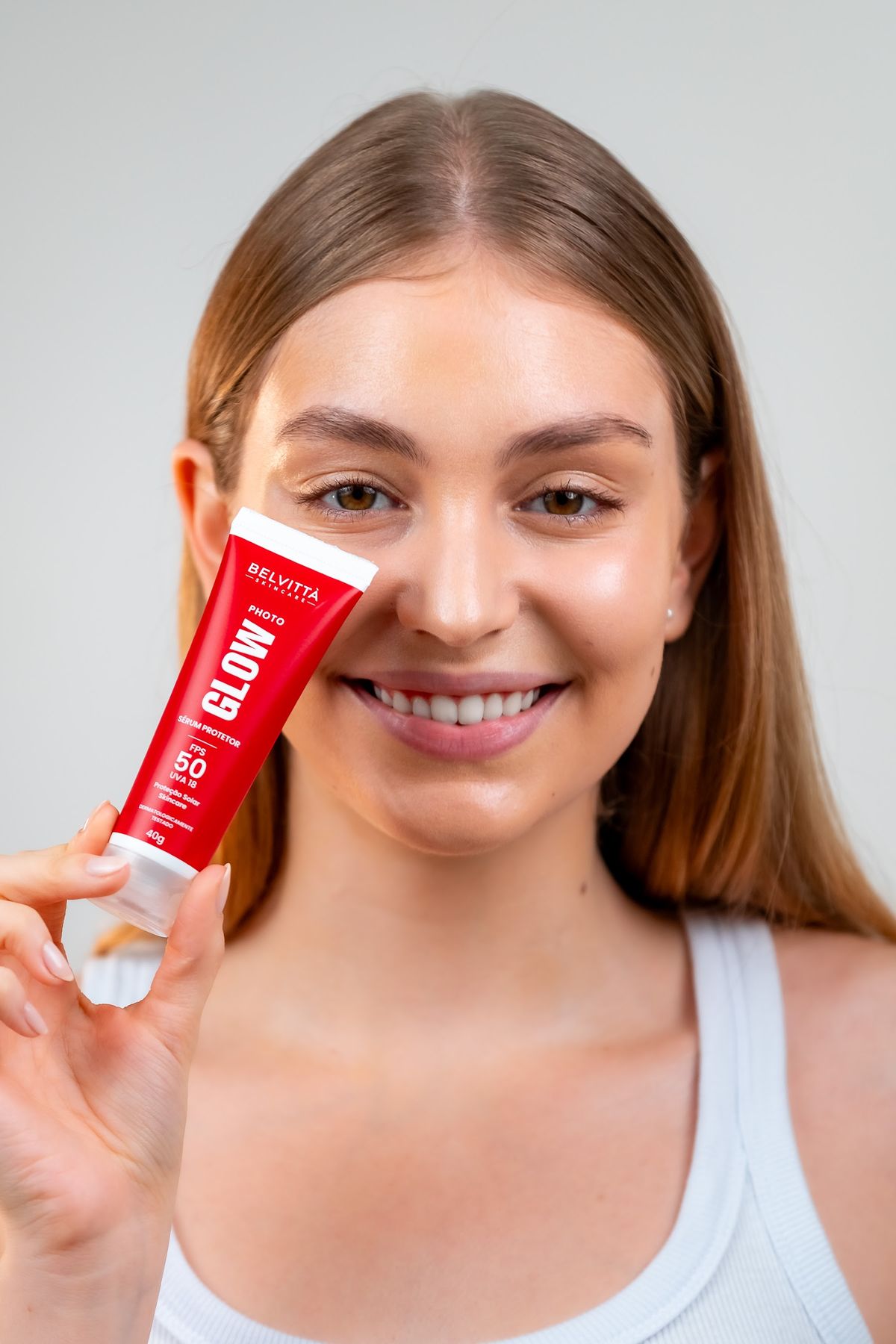 Modelo com o Photo Glow Sérum aplicado, segurando o produto ao lado do rosto