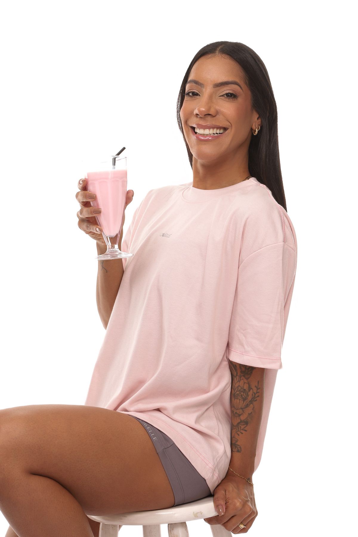 Mulher sorrindo com camiseta oversized rosa e shorts cinza CAVELLE