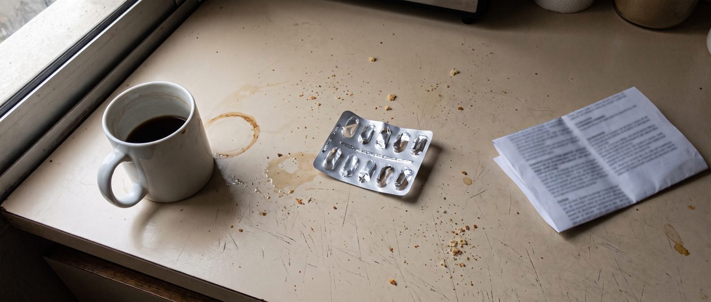 Cafe frio, un blister de vitaminas vacio y un papel de analisis sobre la mesada de la cocina